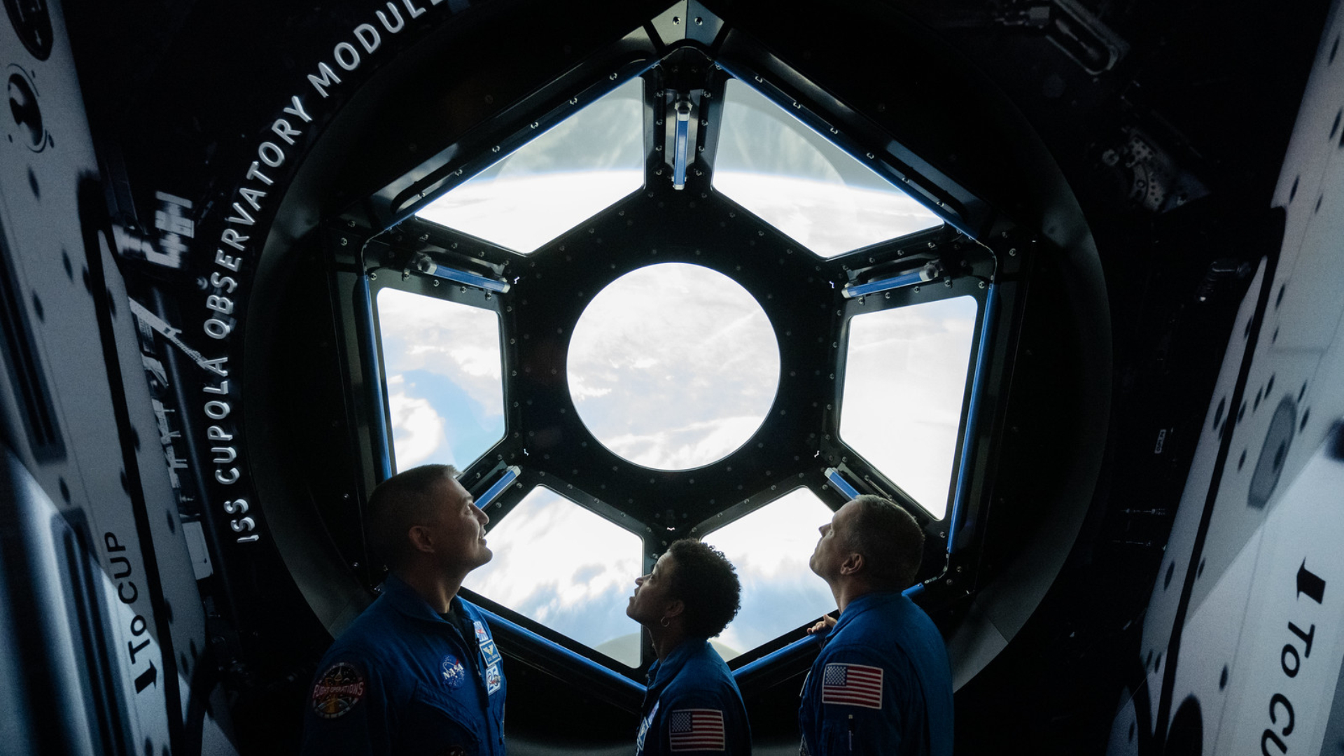 Os astronautas da NASA Kjell Lindgren, à esquerda, Jessica Watkins, ao centro, e Robert Hines, à direita, são vistos na galeria One World Connected olhando para uma recriação interativa da Cúpula da Estação Espacial Internacional. Lindgren, Watkins e Hines passaram 170 dias no espaço como parte das Expedições 67 e 68 a bordo da Estação Espacial Internacional. Crédito da foto: (NASA/Joel Kowsky)
